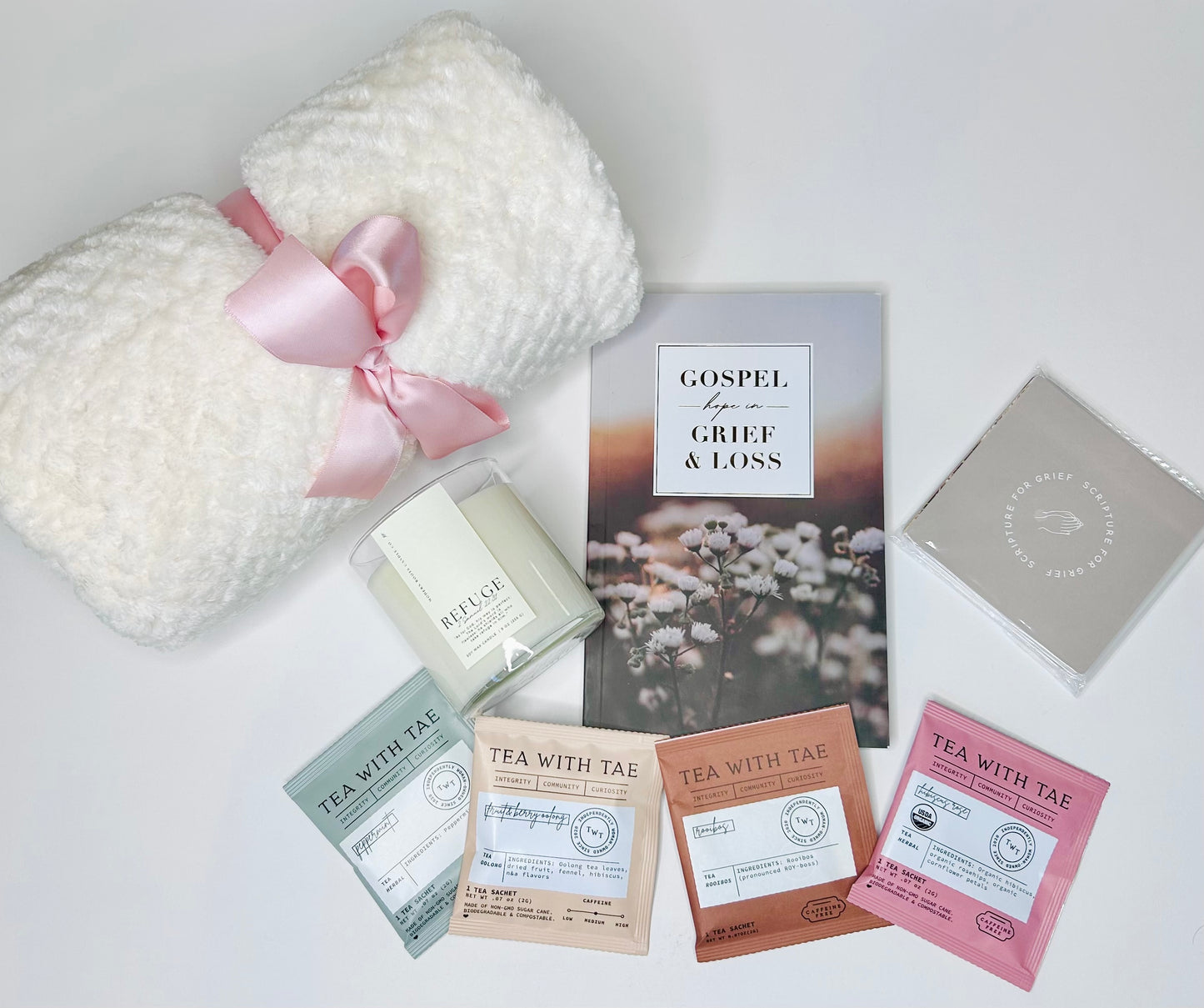 Gift set with tea bags, a blanket, and a book titled 'Gospel of Grief & Loss' on a white surface.
