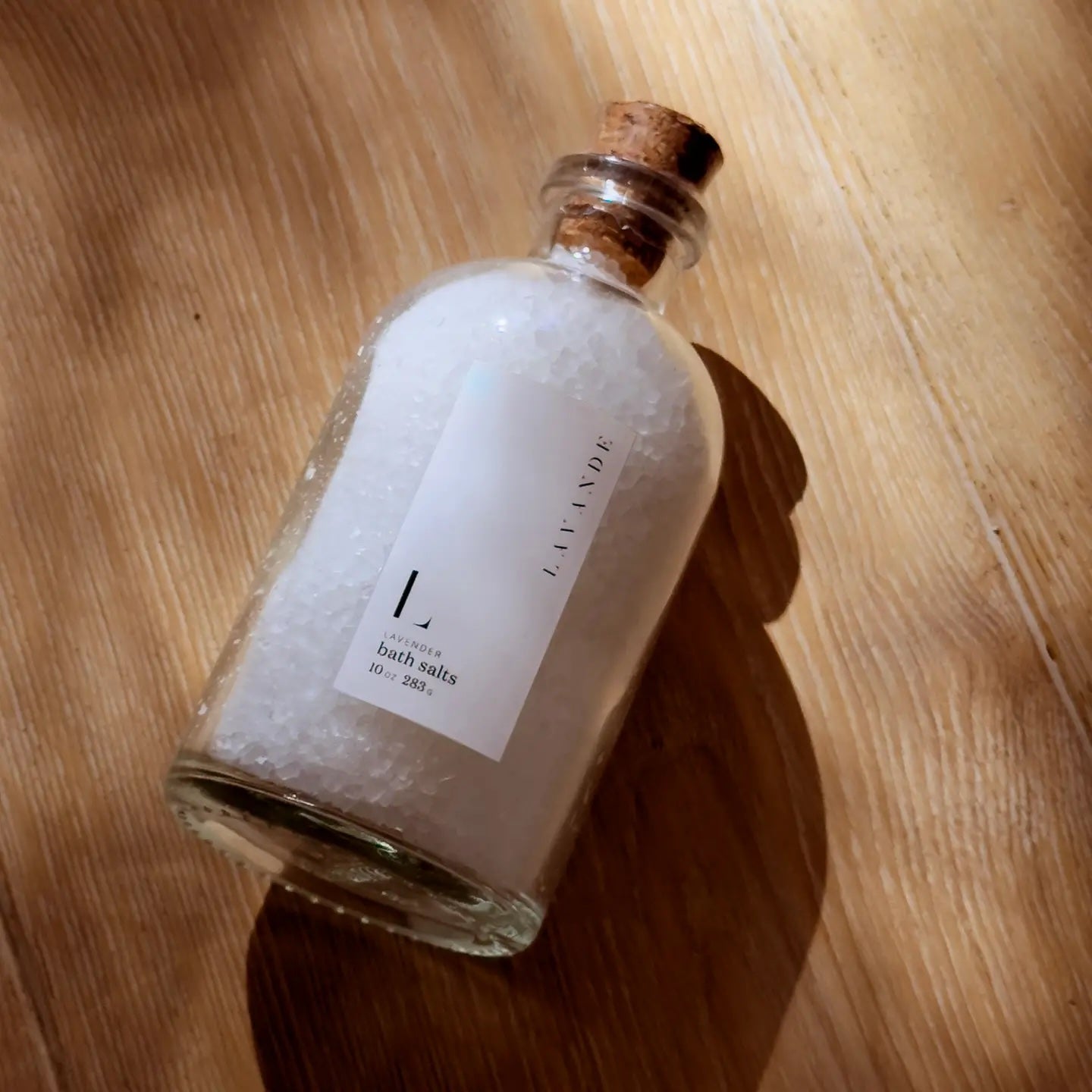 Lavender bath salts in elegant clear glass jar with cork topper, made with coarse mineral sea salt and lavender essential oil for detoxifying skin, relaxation, and silky smooth results