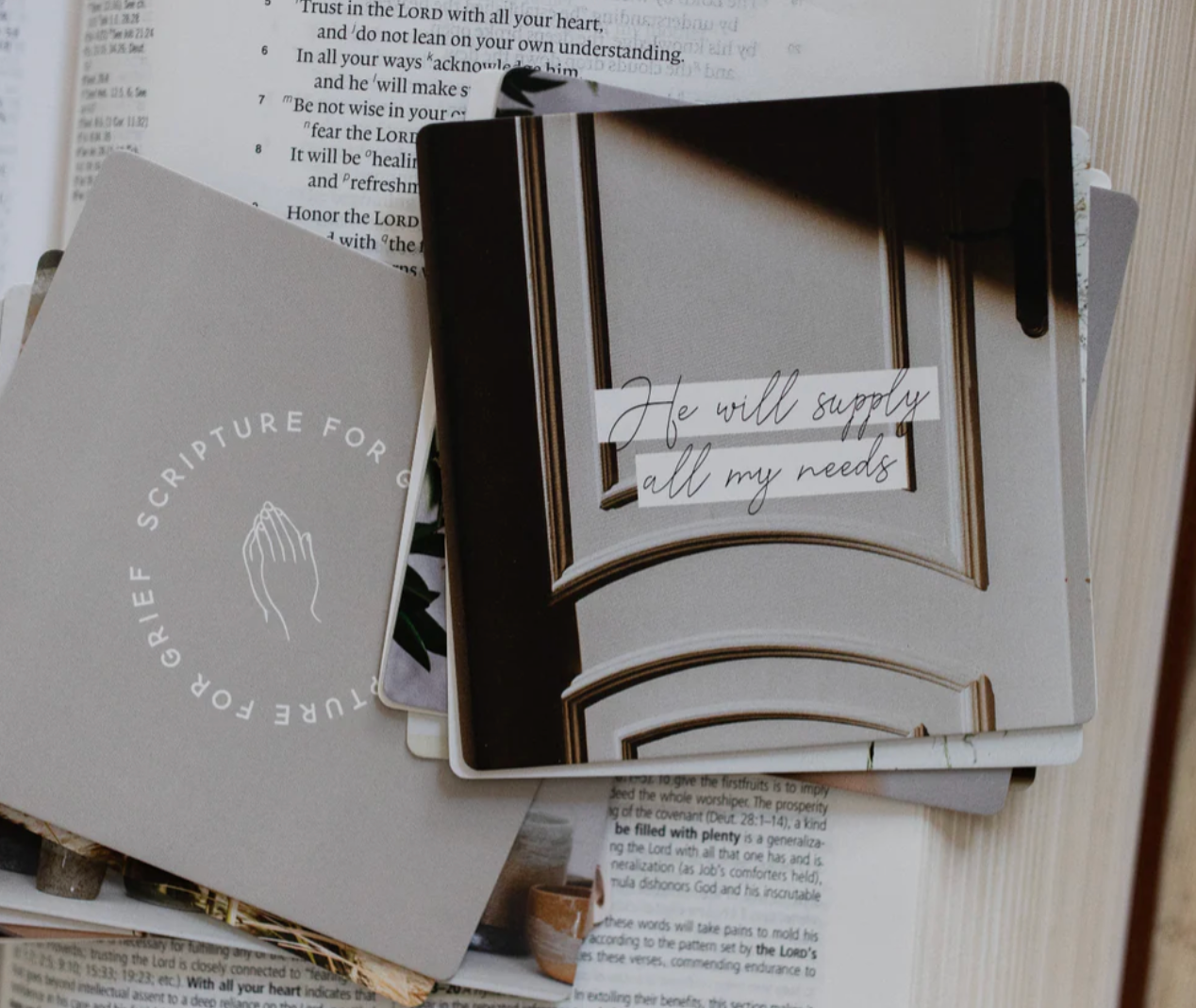 Scripture for Grief verse card displaying 'He will supply all my needs' placed on open Bible, encouraging faith-based comfort card from grief scripture card set
