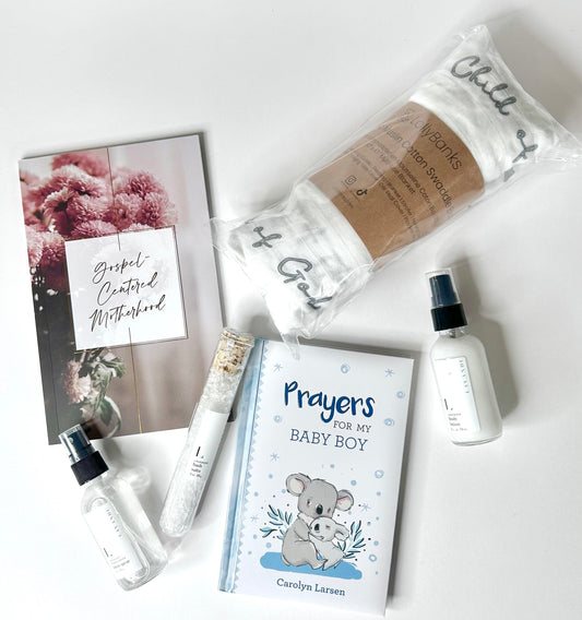 Flat lay of all 6 New Mom & Baby Boy Blessing Box items on white background including Gospel-Centered Motherhood Devotional, Prayers for My Baby Boy Prayer Book, Baby Muslin Swaddle Blanket Child of God, Mini Lavender Bath Salts, Mini Lavender Body Lotion and Mini Linen Spray